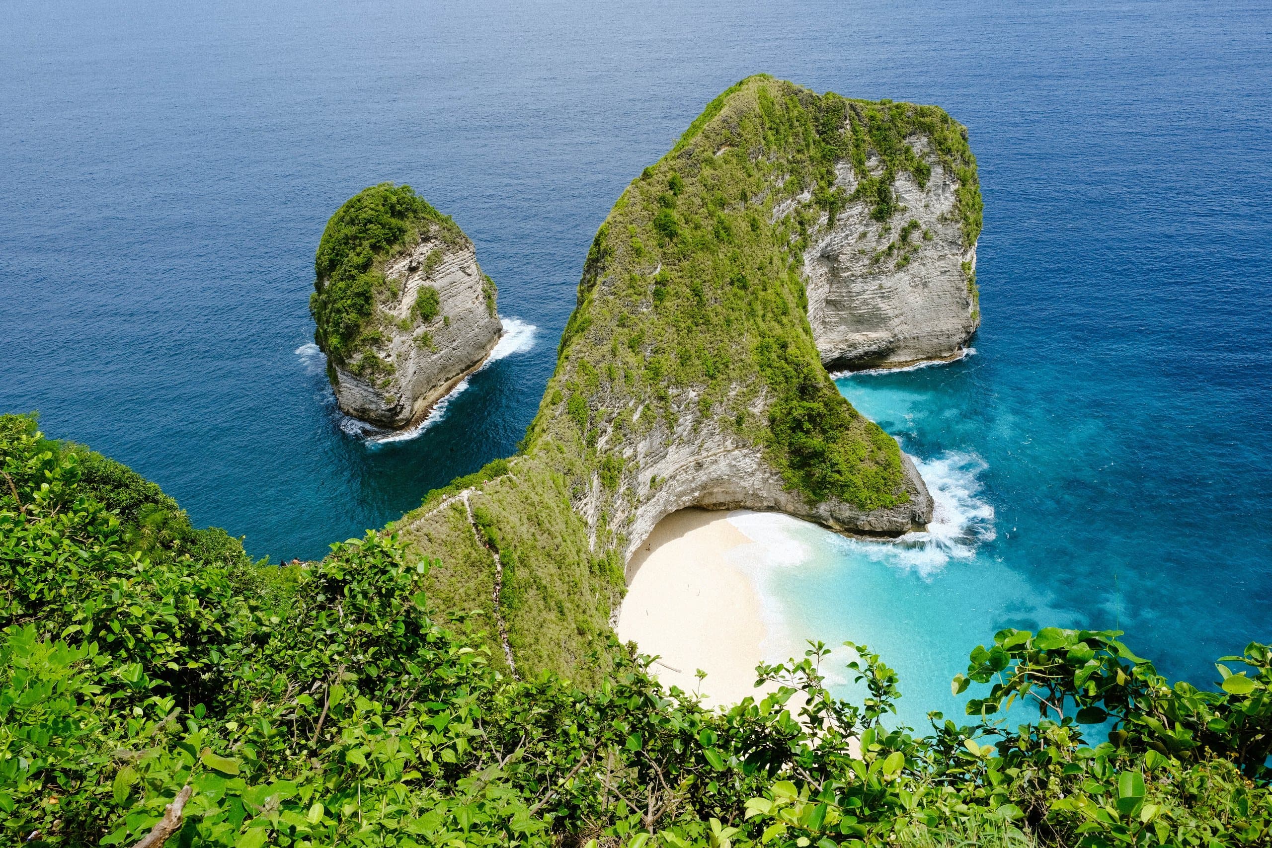 The headland at Kelingking Beach on Nusa Penida, its green cliffs curving around a white sand cove and turquoise water